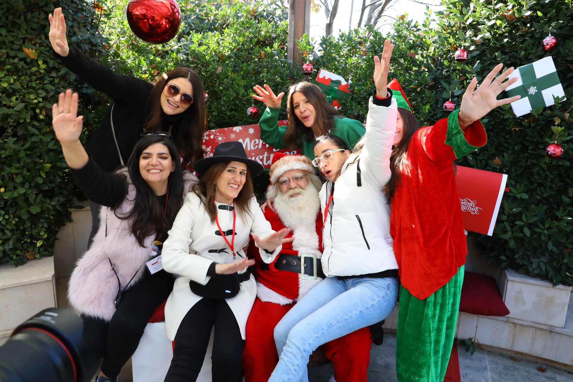 Volunteers and friends pose with Santa in front of the Merry Christmas backdrop