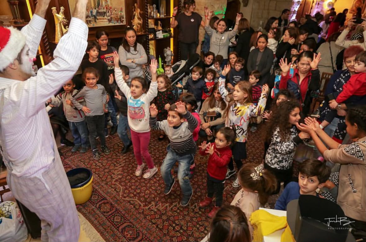 An entertainer in a Santa hat leads dancing children in the stone hall