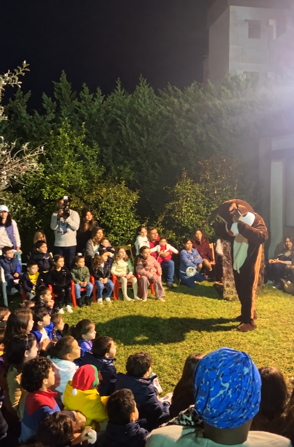 A mascot performs on the lawn for seated children at night